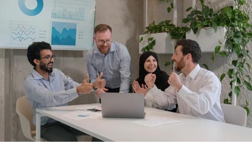 Équipe marketing multiculturelle célébrant le succès d’un projet digital autour d’un ordinateur portable, illustrant la collaboration, la performance web et la transformation digitale en entreprise.