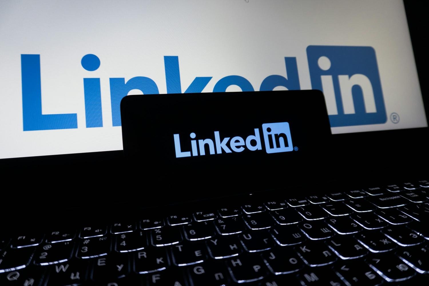 Logo LinkedIn affiché sur l’écran d’un ordinateur portable, avec un smartphone posé devant montrant également le logo LinkedIn sur fond sombre.